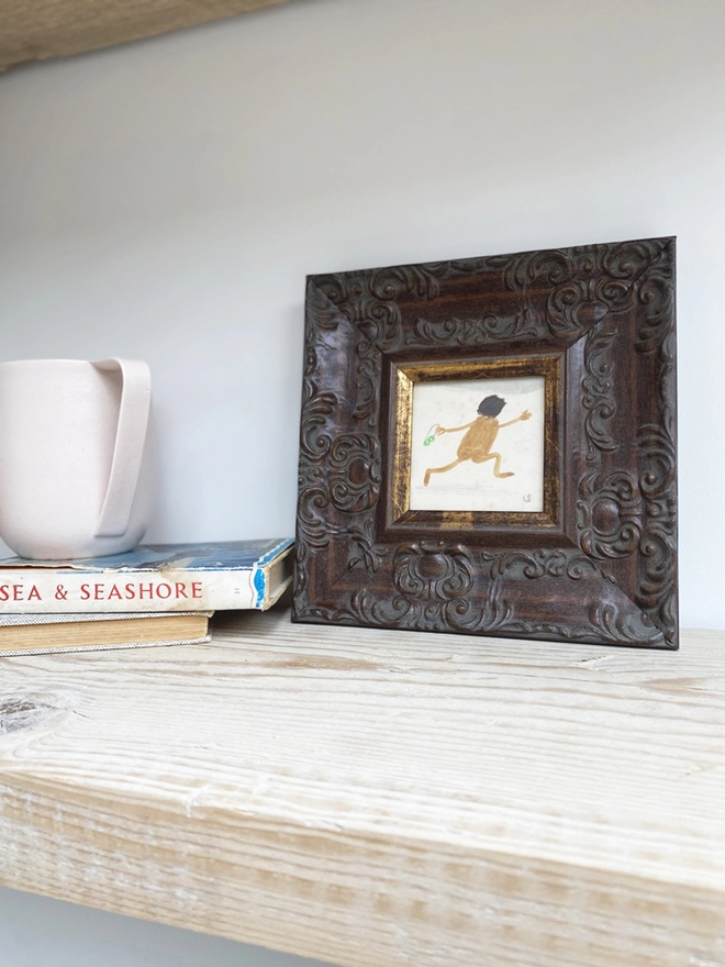 pale wooden shelf with framed drawing of naked man joyfully running on the beach 