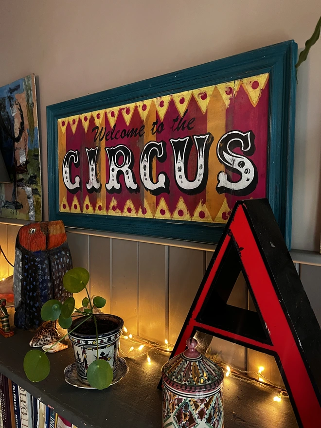 welcome to the circus sign, with colourful stripes of pink, yellow and orange with a teal frame and zig zag pattern at the top and the bottom. surrounded by a teal frame