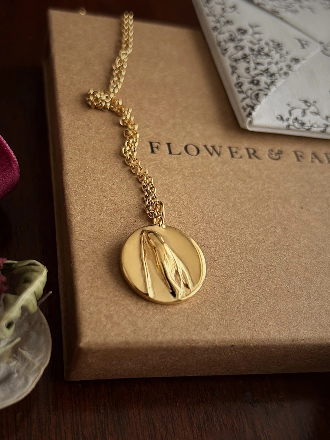 Gold snowdrop coin belcher necklace close up representing hope draped over flower & fable packaging