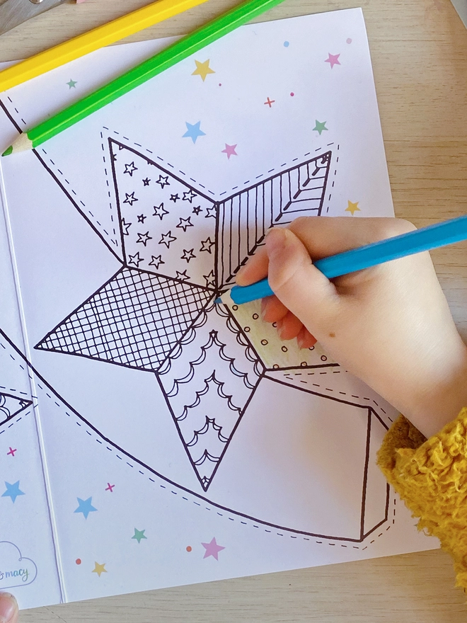 A child is colouring a Christmas greetings card with a star tree topper design.