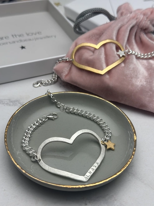 model wears a personalised large open heart charm in silver on chunky curb chain with a small gold star charm, gold version in the background. gift box and pouch