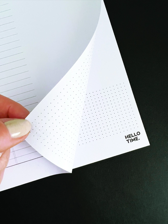Fingers turning over a page from Hello Time's weekly planning pad to reveal the dot grid reverse
