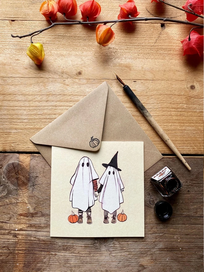 a greeting card featuring an illustration of 2 ghost children with pumpkins laid on a Kraft envelope