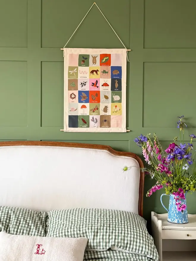 Rainbow Woodland Alphabet Fabric Banner, hanging in a green wall next to a bed. 