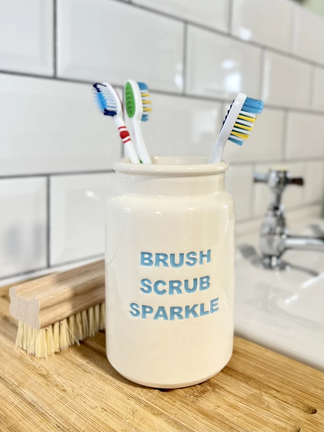 A handmade ‘Brush scrub sparkle’ (lettering in blue) is being used to hold toothbrushes.