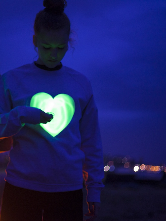 Girl drawing with a penlight onto an illumines heart printed onto a sweat