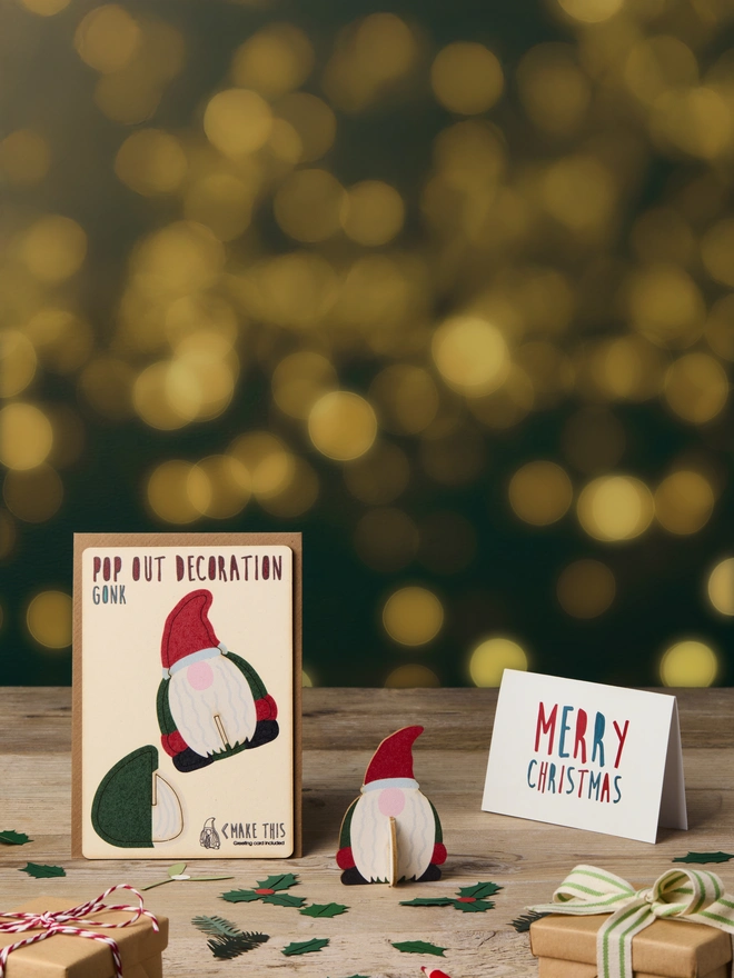 Pop out laser-cut Gonk Christmas decoration and Merry Christmas card and brown kraft envelope on top of a wooden desk