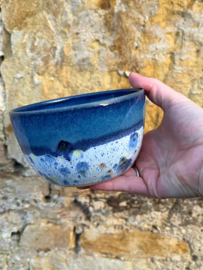 Shoreline Small Bowl, a colourful bowl held in front of a brick wall. 