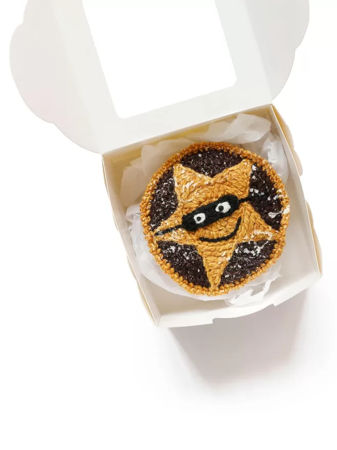 Kate Jenkins' Mince Pie in Disguise seen wearing a black eye mask in a cake box.