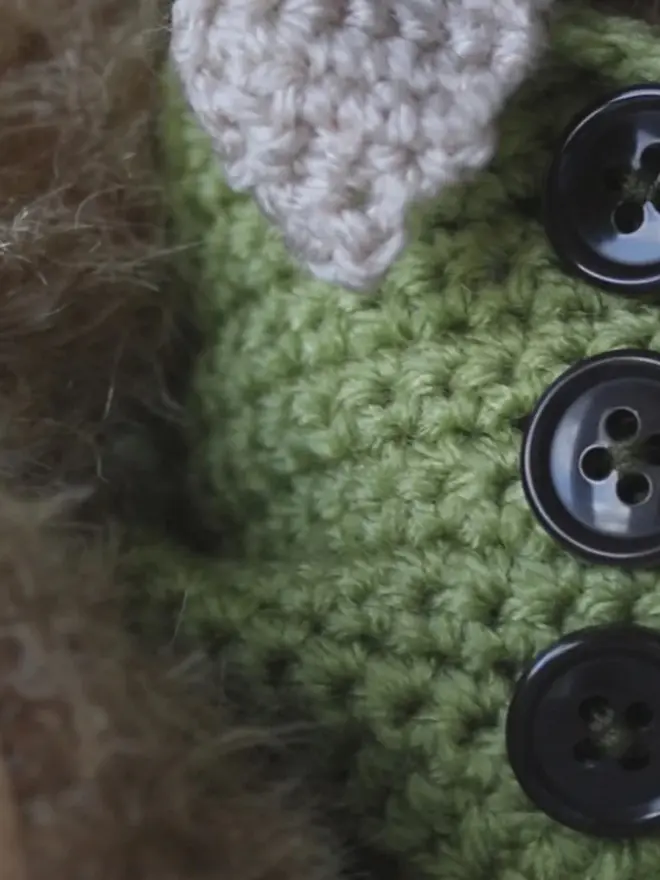 Handmade brown teddy bear with a white scarf wearing a green cardigan, sitting against a plain background.