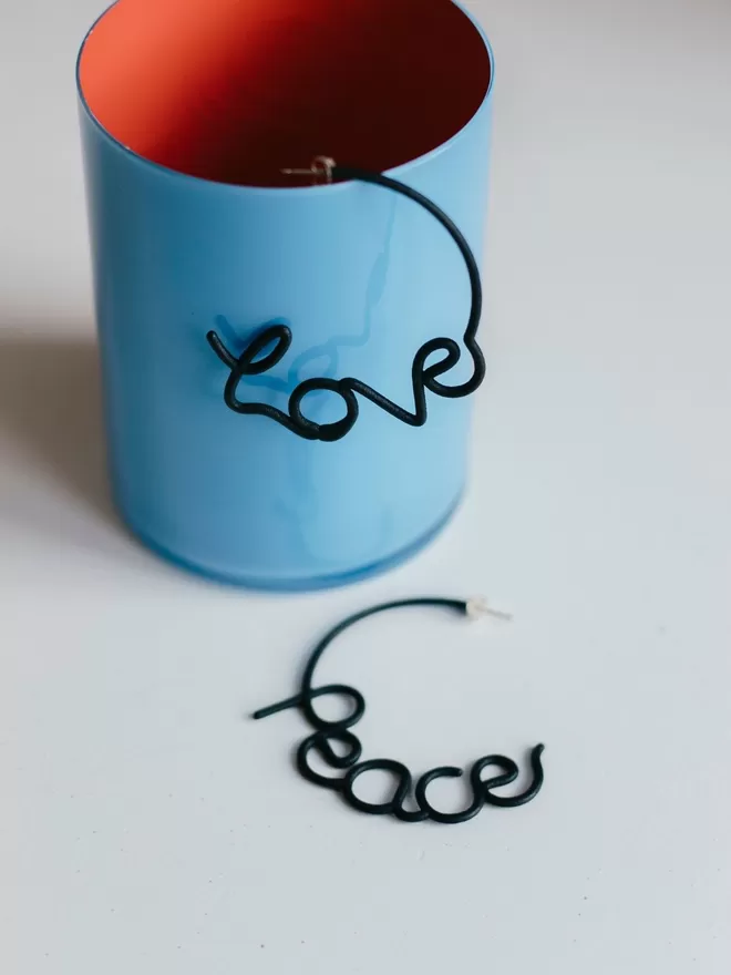 Love and Peace black large earrings seen in a blue cup with a red inside.