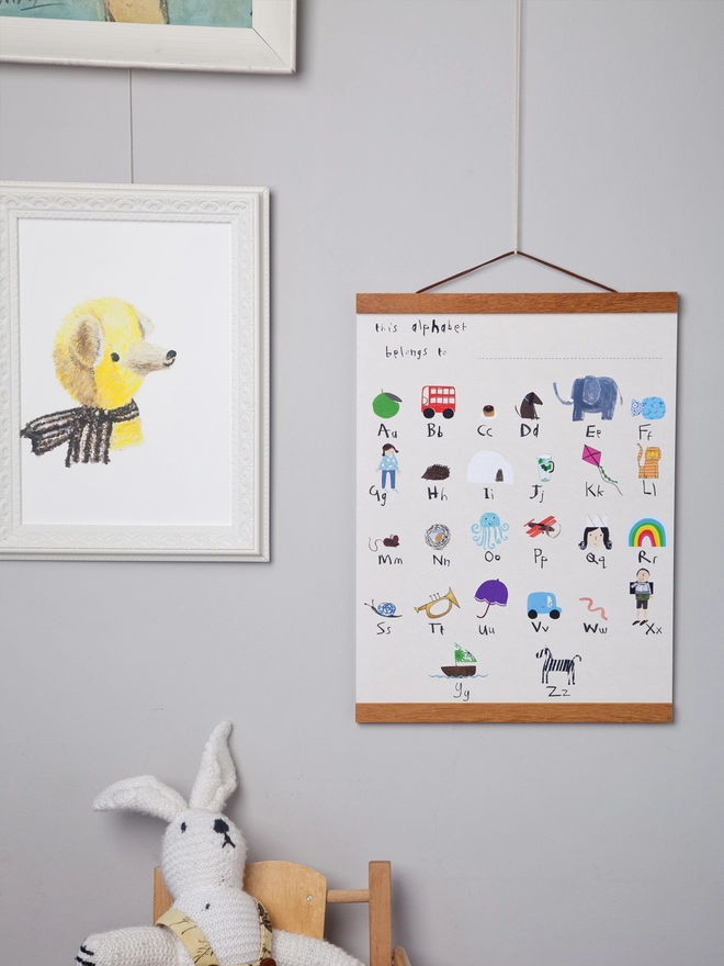 grey wall with alphabet poster hanging on oak poster hanger next to soft toy and framed pictures