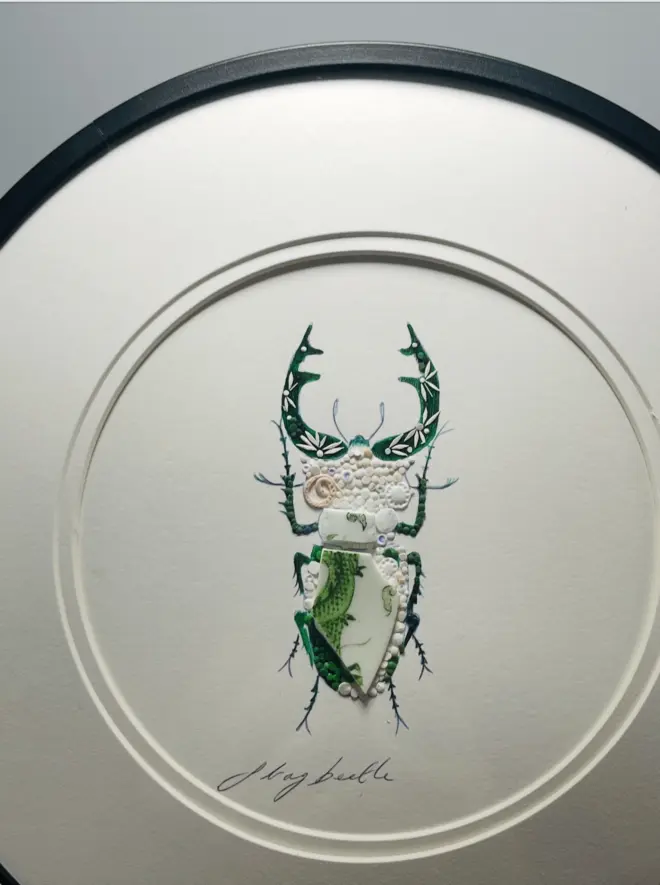 Hand-drawn, painted, mosaic clay, green Dragon pottery insect on white double mounted card, in a black circular frame.