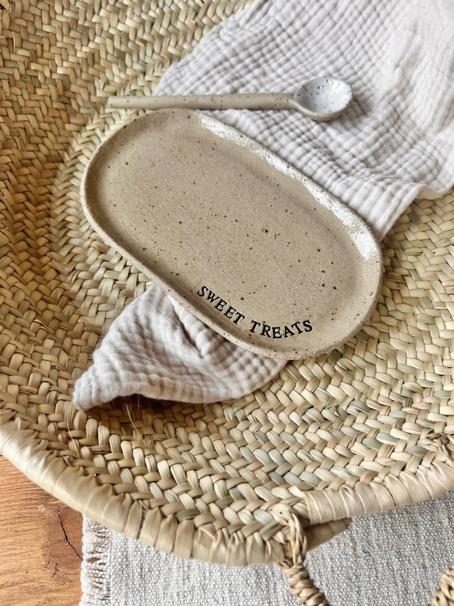 Oval ceramic plate laid on a white tea towel, with the words 'sweet treats' stamped around the edge
