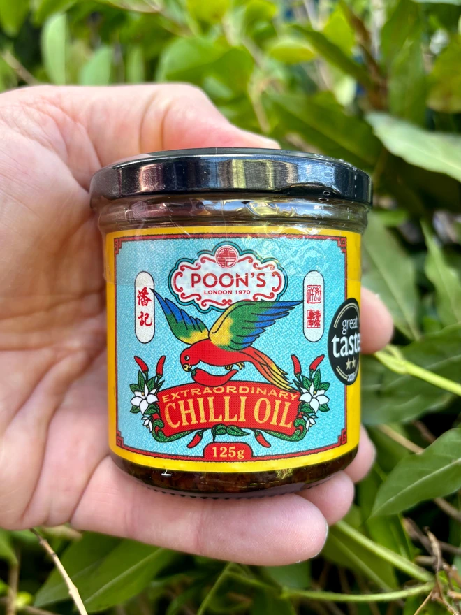 Poon's Extraordinary Chilli Oil being held in front of a background of plants