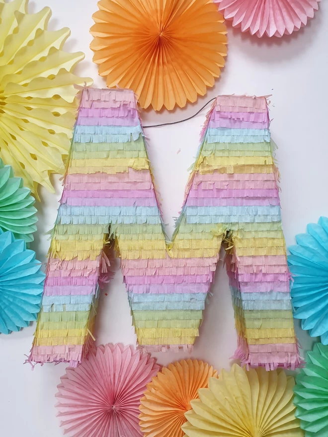 pastel stripe letter M pinata by Pinyatay on a background of paper decorations