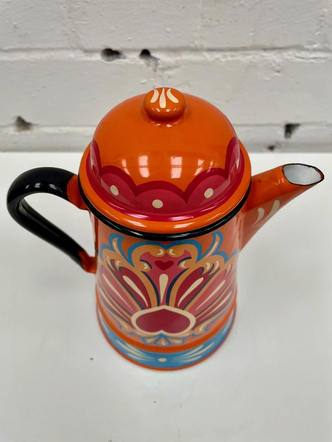 Lid of orange coffee pot, featuring a pink and red scalloped design.