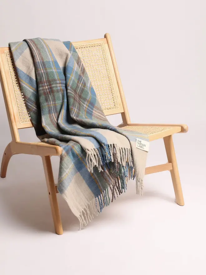 Stewart Muted Blue Blanket, a blanket draped over a wooden chair on a plain surface against a white backdrop. 