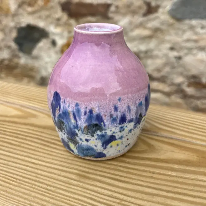 Shoreline Bud Vase, a colourful vase placed on a wooden surface against a brick backdrop. 