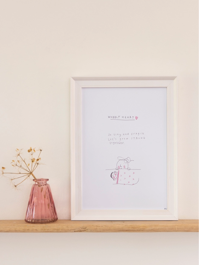 An illustration of a lady peeping over a sleeping baby in a white frame next to a pink vase with foliage in it. Text on picture reads "Wobbly heart"