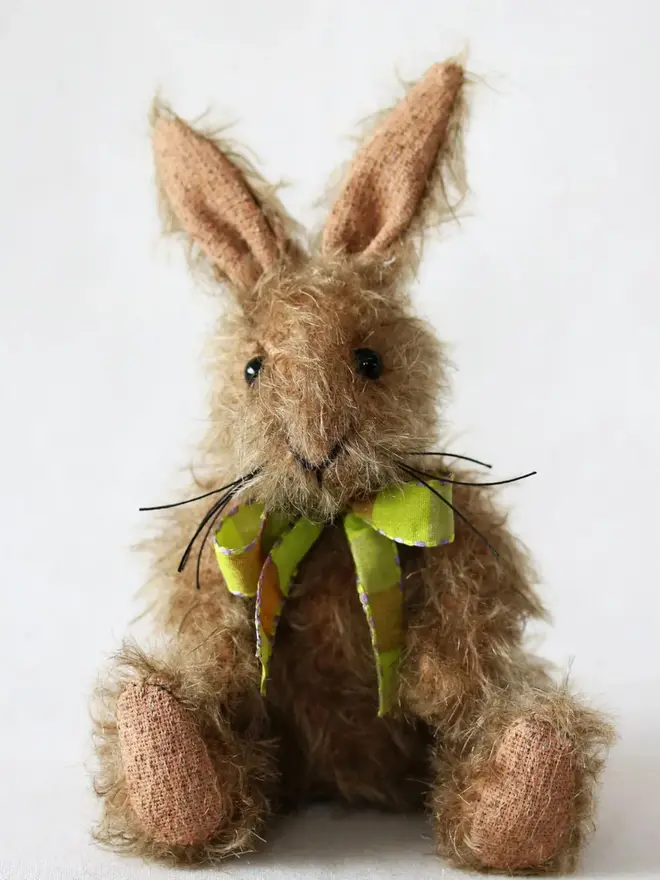 Handmade brown stuffed rabbit with long ears and a green ribbon bow sitting upright against a plain background.