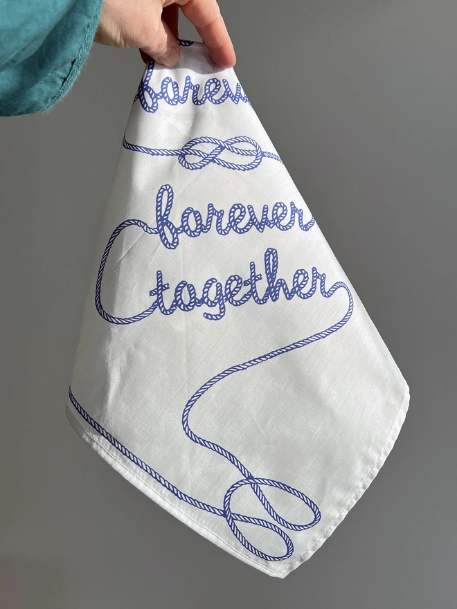 A white hand holds a Mr.PS Together Forever Handkerchief against a sunlit wall