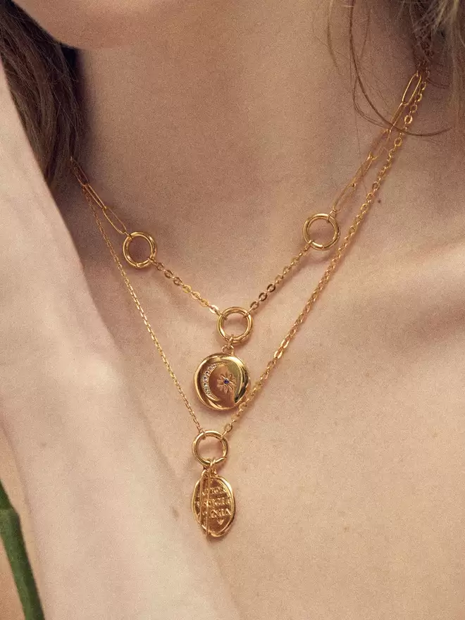 Woman wearing two gold necklaces styled with a gold locket and a love medallion