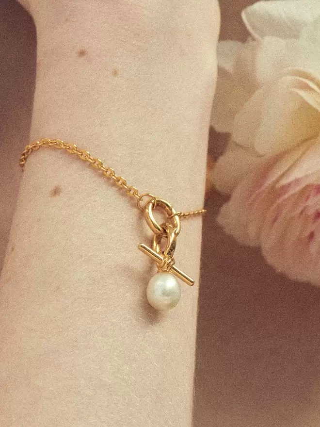 woman wearing a gold bracelet styled with a pearl amulet and a mini Albert lock charm
