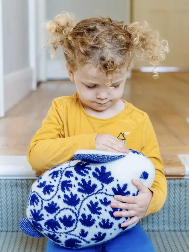 child in yellow shirt holding blue and white plush rabbit