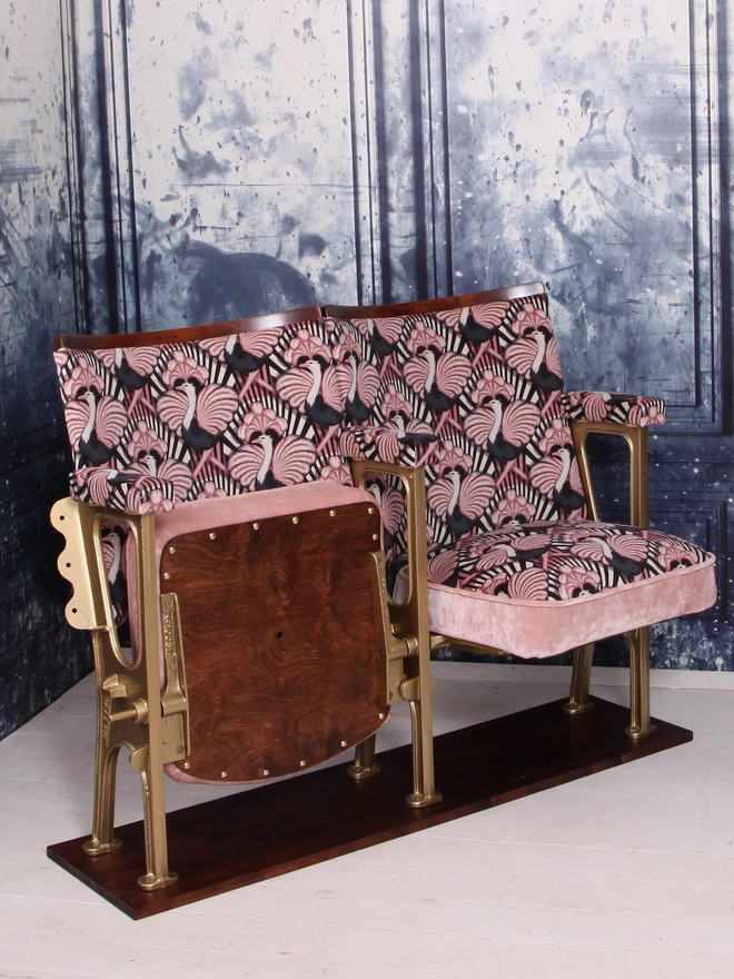 Set of two vintage cinema seats upholstered in a pink ostrich Art Deco design velvet with pink panel and piping against a blue marbled wall.  One seat is down and one seat is flipped up