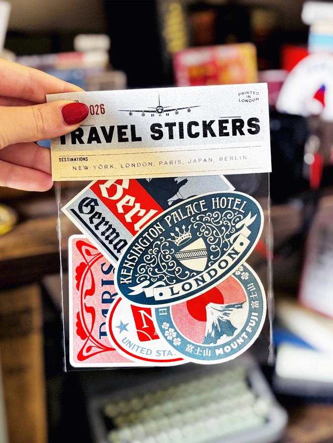 Vintage Travel Stickers for New York, Japan, Paris, London and Berlin in a cellophane bag, bookcase blurred in background 