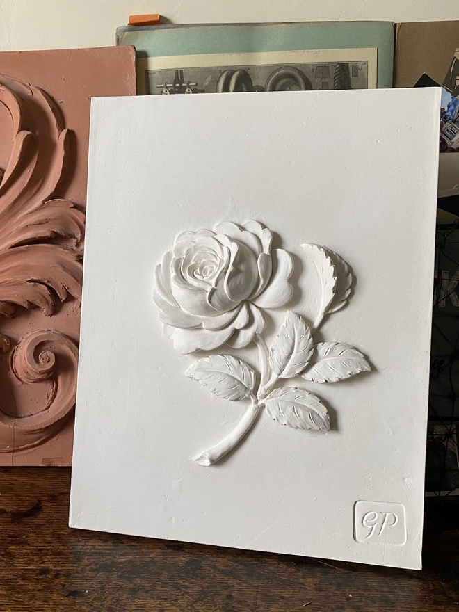 Decorative plaster wall plaque with Old Garden Rose design on a table with scrapbook and maquette behind