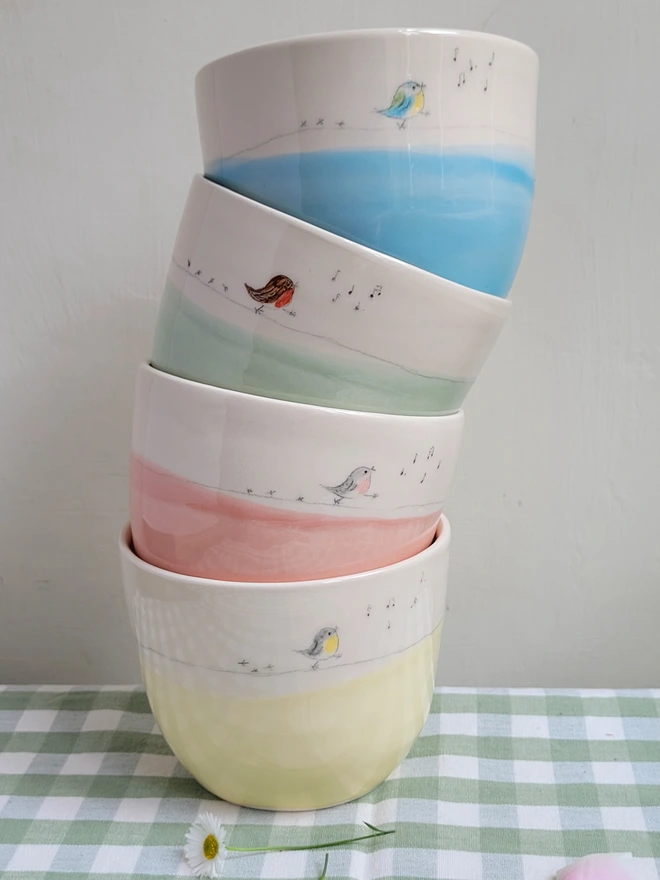 stack of colourful pastel ceramic beakers with robins, robin red breast and blue tit birds painted walking around the cup with musical notes bird song and bird prints