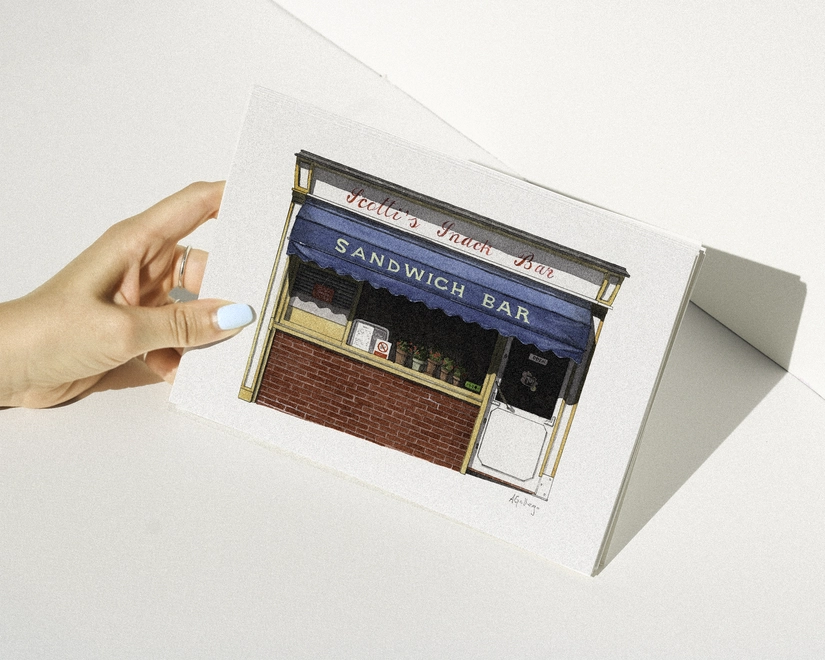 A hand with blue nail polish holding a print featuring an illustration of the Scotti's Sandwich Bar against a white background.