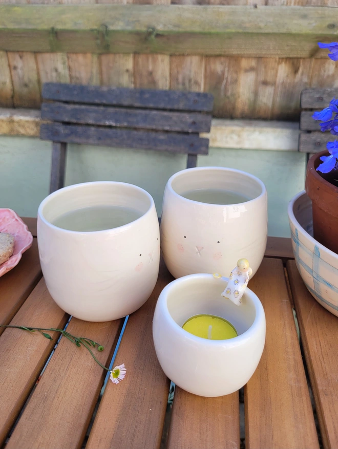 2 bunny beakers in  off white ceramic on a table outside filled with drinks with a tealight candle in the foreground 