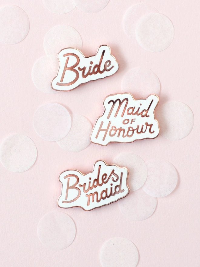 bridesmaid, bride and maid of honour enamel pins laying on pink confetti background