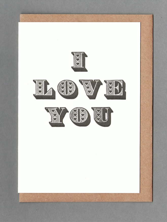 White card with black text reading 'I LOVE YOU' with a kraft envelope behind it