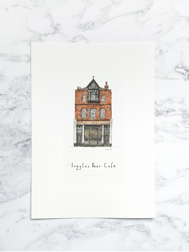 Beautiful watercolour illustration of Fuggles in Tonbridge.  A brick building with a dark framed shopfront that has a large window and wooden fascia sign above with ‘Fuggles Beef Cafe’ written in black lettering. The watercolour style is painted with a black pen outline and organic loose style with small details. The print is a small illustration on the centre of a white page and the paper sits on a white marble background.
