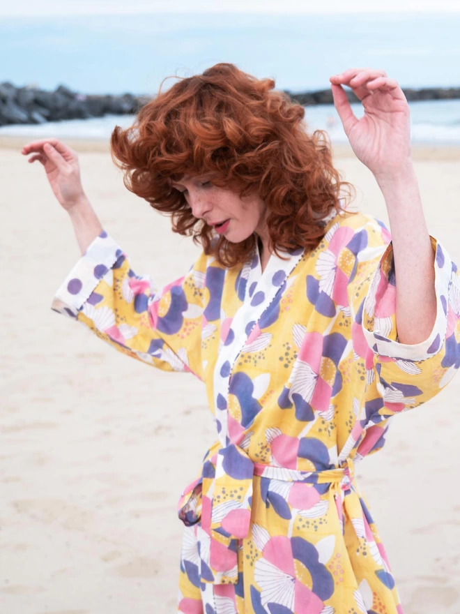 Red haired girl dancing on beach wearing a block printed yellow robe in a large scale floral design