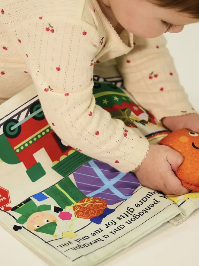 Baby holding sudsy orange toy with xmas newspaper below