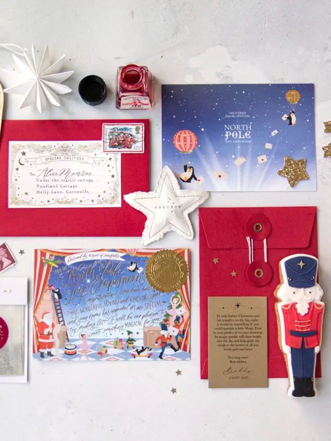 The full letter from Father Christmas kit laid flat: a stamped red envelope with a personalised label, the starry blue "North Pole Toy Emporium" card back, the illustrated notecard with a gold seal, and a red string-and-washer envelope with a kraft instruction card. A felt "Believe" star and a nutcracker biscuit sit alongside.