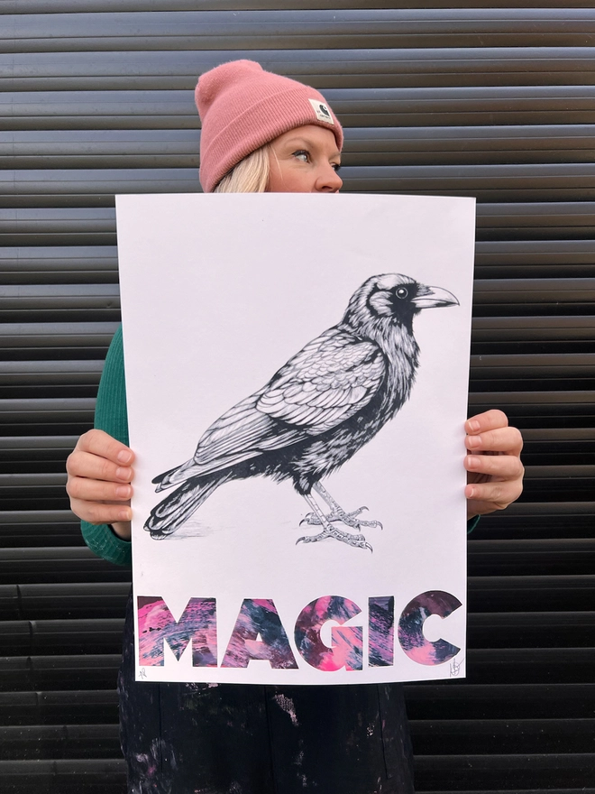 woman artist holding original unique art, of a crow with the word magic underneath, screen print with mono print, 