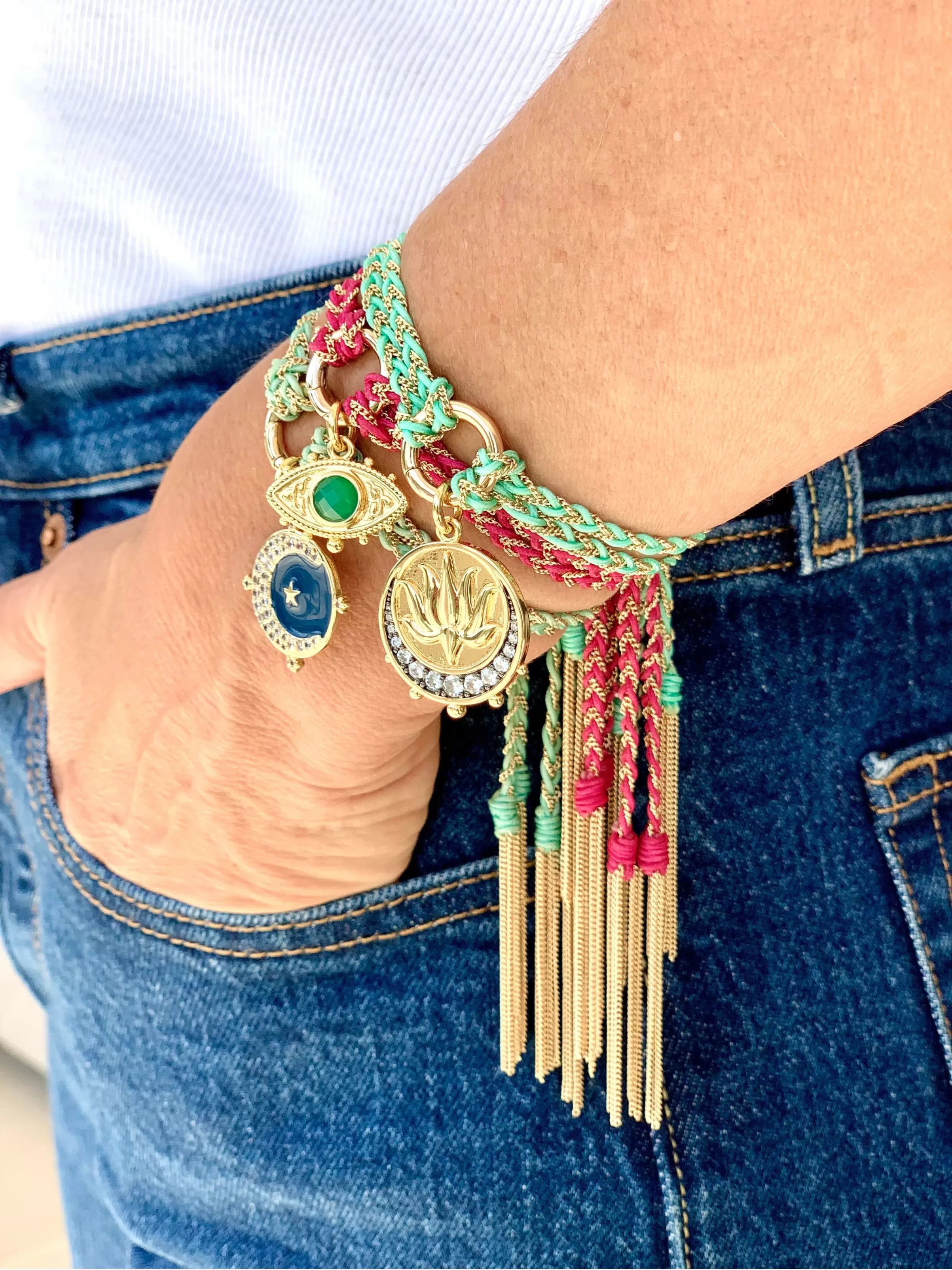 Woman wearing a stack of gold turquoise and pink friendship bracelets strung with colourful gold talisman charms
