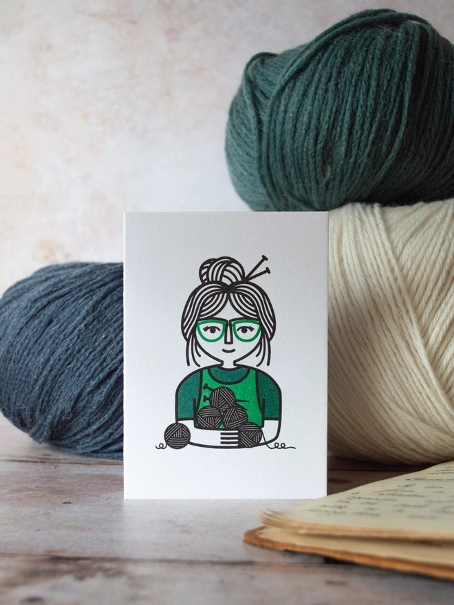 A bold illustration of a knitting character enjoying their fabric and craft based hobby surrounded by balls of wool.
