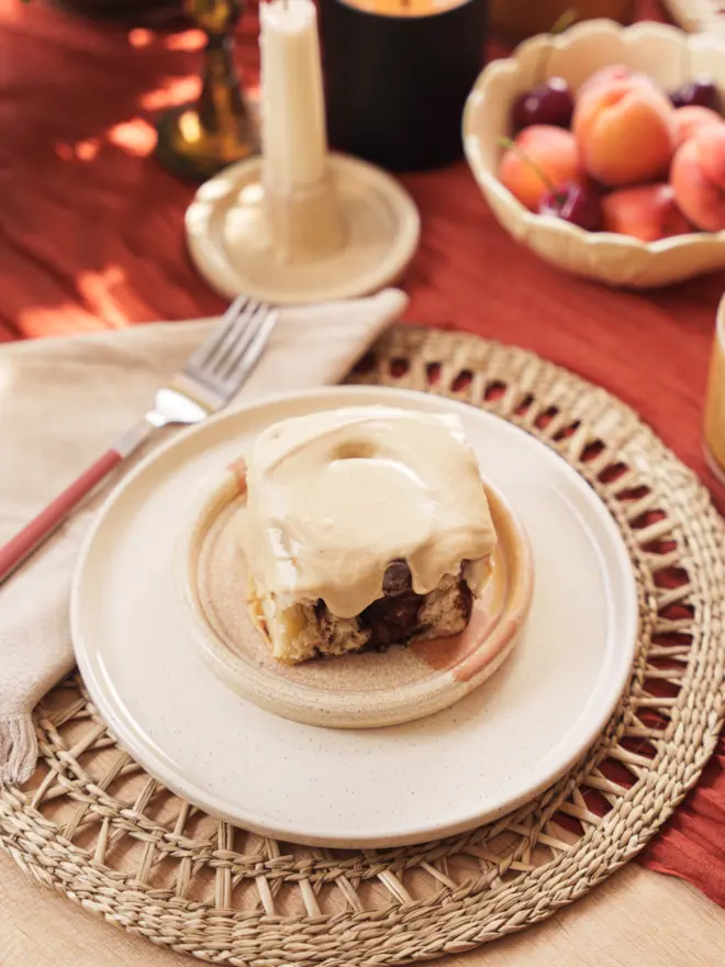 a single Latte Cinnamon Bun on a plate with some apricots in the background