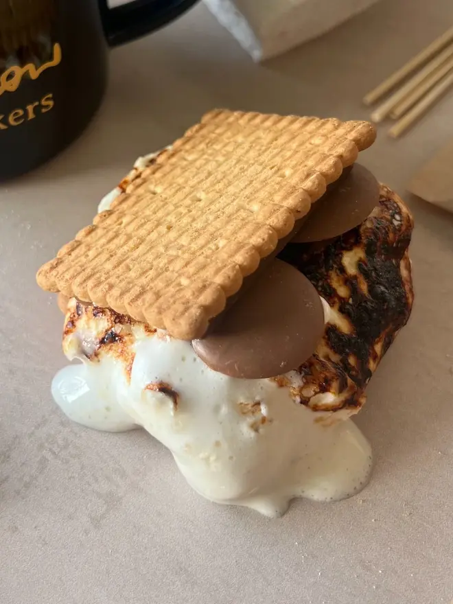 Luxury S'mores & Hot Chocolate Kit, a melter with a marshmallow stuffed inside on a marble surface. Behind, the skewers used. 