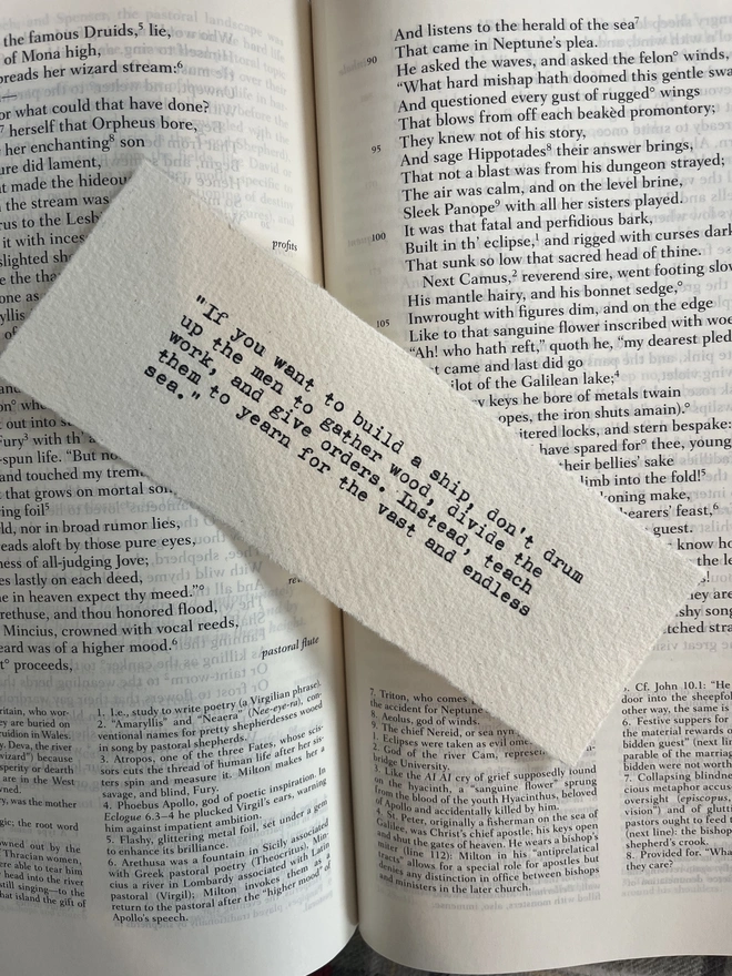 A handmade cotton rag paper bookmark with deckled edges, featuring a custom quote typed in black ink with a vintage antique typewriter.