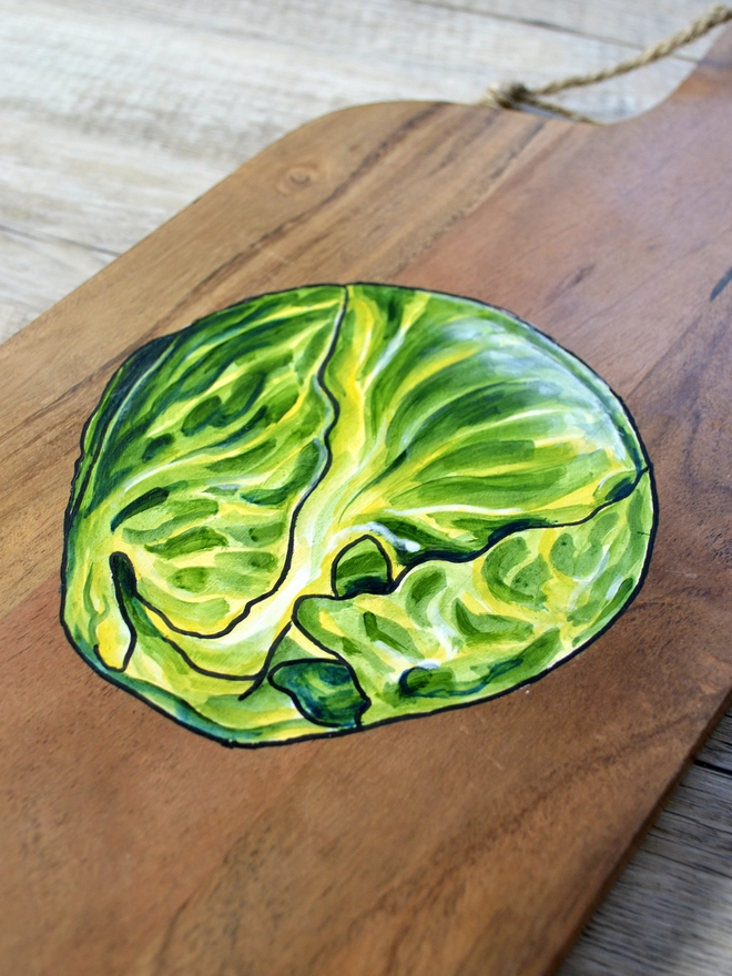 A wooden serving board with a handpainted design of Brussels sprouts