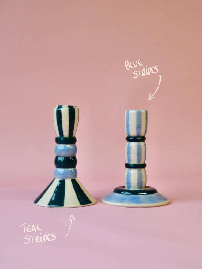 Handmade ceramic candlesticks with blue and teal stripe patterns, featuring a teal striped design on the left and a soft blue striped candlestick on the right, displayed on a pink background.