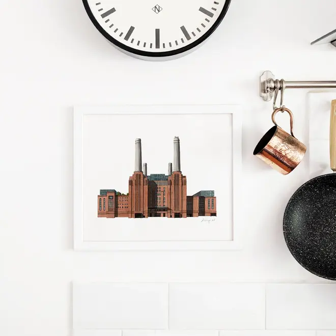 Battersea Power Station Giclée Print (Unframed), a print of Battersea Power Station sitting in a white frame against a plain backdrop. It is joined by a clock. 